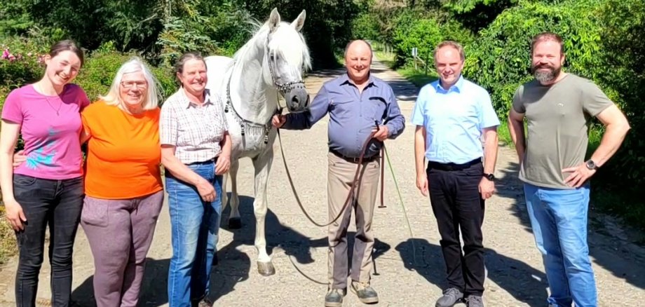 Ein weißer Araberhengst zeigt sich in traditionellen Zaumzeug mit dem Team des Arabergestüts Kauber Platte (insgesamt fünf Personen) und Bürgermeister Mike Weiland. 