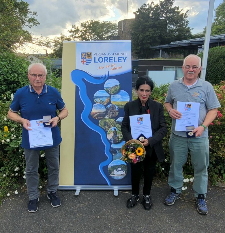 Klaus Itzel, Gertrude Stoy-Niel und Karl-Heinz Goerke wurden für ihr jahrzehntelanges ehrenamtliches Engagement mit der Ehrenmedaille des Bürgermeisters der Verbandsgemeinde Loreley geehrt und präsentieren nebeneinander stehend ihre Urkunden.