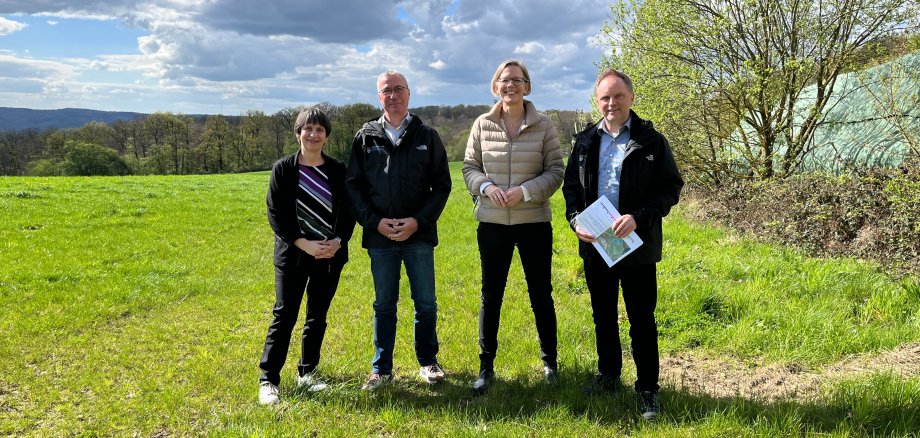 von links nach rechts stehen Referatsleiterin Dr. Stefanie Hahn, Bauamtsleiter Gerd Schuster, Staatssekretärin Simone Schneider und Bürgermeister Mike Weiland an einer potenziellen Fläche zur Errichtung einer Photovoltaik-Freiflächenanlage. Das Wetter ist sonnig und im Hintergrund sind Bäume und Berge zu sehen.