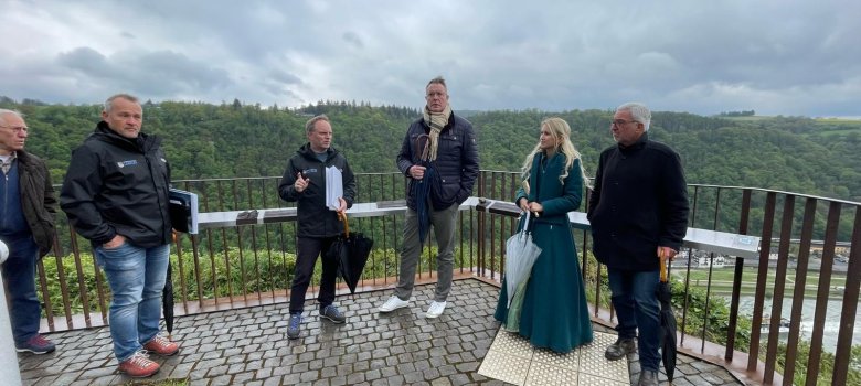 Ein Bürger, Projektleiter Armin Schaust, Bürgermeister Mike Weiland, Staatsminister Schweitzer, die Loreley-Repräsentantin Katharina Blanckart und Landtagsabgeordneter Roger Lewentz stehen an der Felsspitze. Das Wetter ist leicht bewölkt und Bürgermeister Mike Weiland scheint gerade etwas zu erklären.