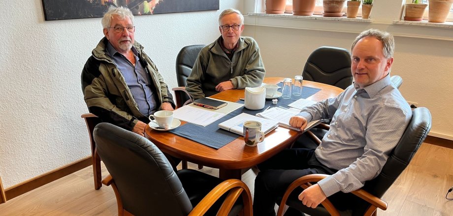 Zwei männliche Vertreter der Bürgerinitiative und Bürgermeister Mike Weiland sitzen an einem Besprechungstisch. Auf dem Tisch sind Kaffeetassen und verschiedene Unterlagen zu sehen.